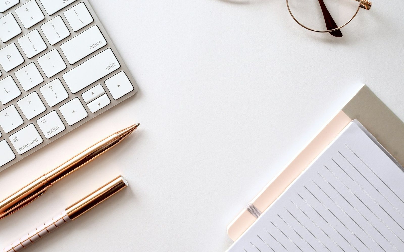 A notepad, pen and glasses on a pale desk