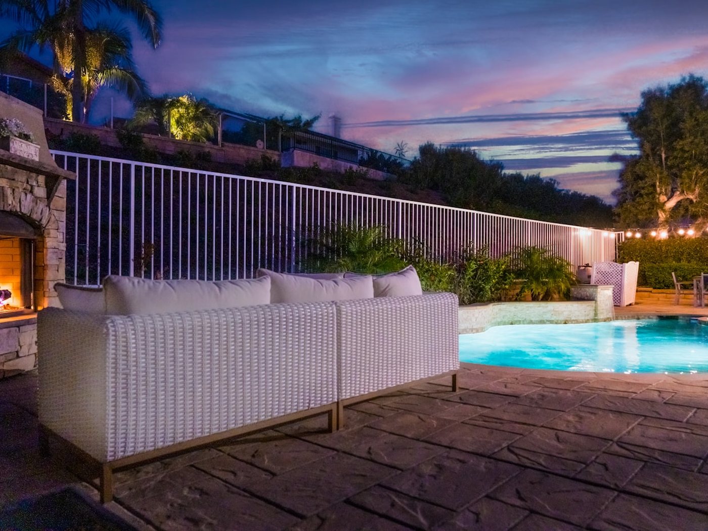An outdoor seating area with a fire feature and string lights at dusk